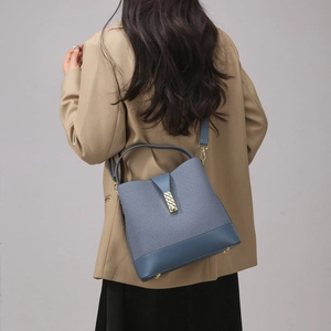Blue canvas bucket bag detail with leather trim and gold decorative buckle on a model