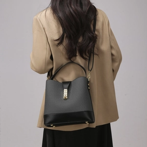 Detail view of a grey canvas bucket bag with black leather trim worn over a beige suit jacket