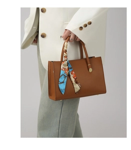 Détail d'un sac cabas en cuir marron avec un foulard en soie coloré sur la poignée