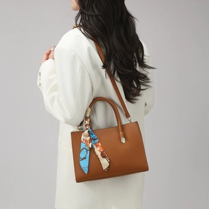 Détail du sac à main en cuir marron avec foulard en soie et finitions métalliques dorées