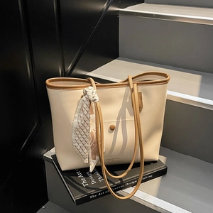 Minimalist beige tote bag with brown leather trim and silk scarf on modern stairs