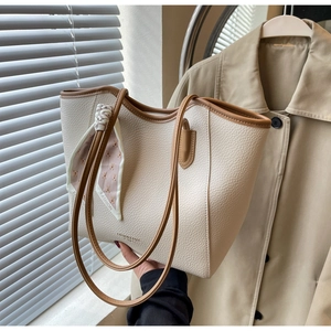 Close-up of cream textured tote bag with brown trim and a pink teddy bear scarf detail