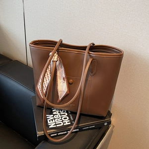 Large dark brown leather tote bag with a decorative silk scarf on a book