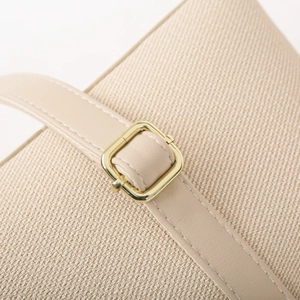 Close-up of beige woven fabric bucket bag with smooth leather strap and gold buckle