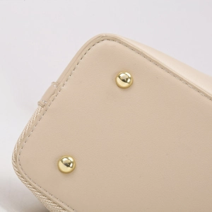 Detail of beige leather bucket bag with woven texture, golden metal feet, and neat stitching