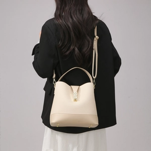 Rear view of model wearing a beige bucket bag with adjustable strap and gold hardware