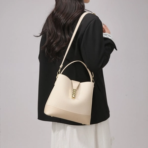 Detail view of the beige bucket bag with contrast leather trim and a gold wavy metal buckle