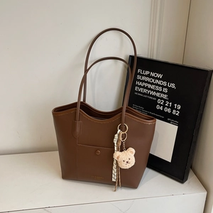 Brown leather tote bag with long shoulder straps and a cute cream teddy bear charm