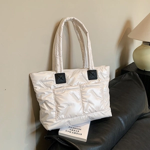 Quilted white down tote bag for women with dual pockets on a black leather sofa