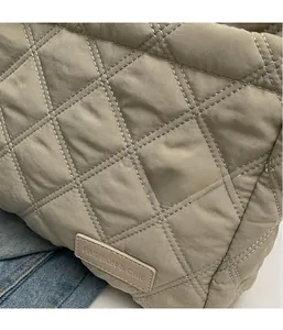 Macro detail of beige quilted nylon crossbody bag with a brown leather logo patch