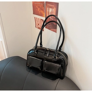 Detail of black glossy faux leather shoulder bag featuring dual pockets and gold zippers