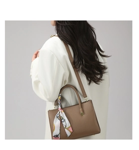 Brown leather tote with decorative silk scarf handle shown on a white oversized blazer