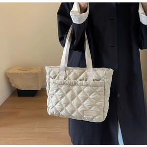 Detail of beige quilted tote bag with classic diamond stitching and wide fabric handle