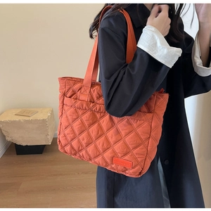 Detail of orange quilted tote bag featuring diamond stitching and rectangular brand label