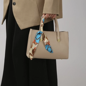 Detail of lychee pattern leather tote bag with colorful silk scarf on handle and metal feet
