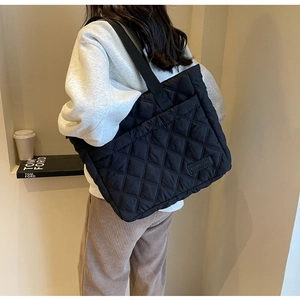 Quilted black nylon tote bag with logo patch detail worn by a model in a minimal setting