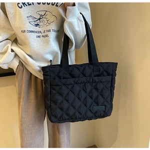 Detail of a black quilted tote bag with diamond stitching and nylon shoulder strap