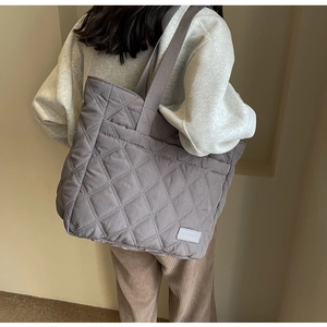 Detail of smoke gray quilted tote bag featuring a stitched fashion label and puffy texture