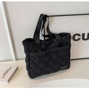 Detail view of a black quilted tote bag with diamond pattern and woven handles on a table