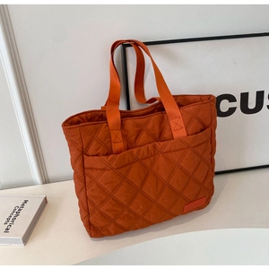 Detail of orange quilted tote bag featuring a buckle outer pocket and nylon web handles