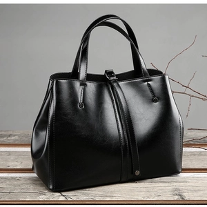 Minimalist black PU leather tote bag with double handles on a vintage wooden surface