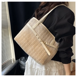 Detail of straw woven tote with cream leather trim and gold buckle on a model