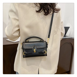 Close-up of black crossbody bag with retro stone texture and gold clasp on a beige suit