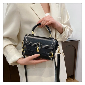 Detail of black leather handbag featuring ivory contrast stitching and gold metal clasp