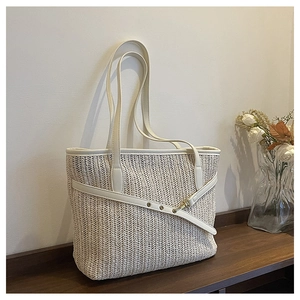 Straw woven tote bag detail showing leather trim and buckle on a rustic wooden shelf