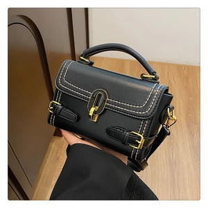 Detail of black crossbody bag with white stitching and gold metal oval lock hardware