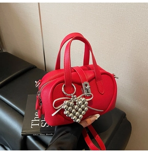 Close-up of red lychee texture handbag with silver heart charm and bow detail