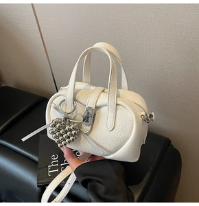 Detailed shot of a white mini Boston bag featuring a silver lock and heart bead charm