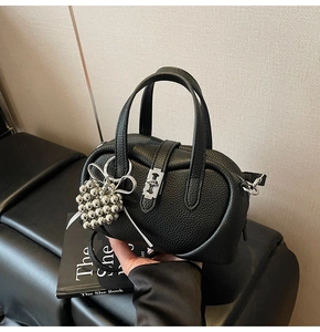 Detailed macro view of black lychee grain leather handbag with silver heart charm and bow