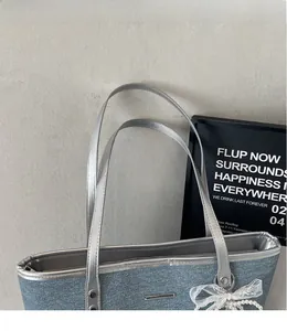 Détail du sac cabas en denim avec anses argentées, nœud en dentelle et breloque perle