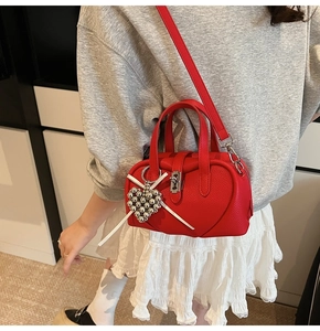 Close-up of heart-shaped red leather bag with silver bead charm and litchi texture