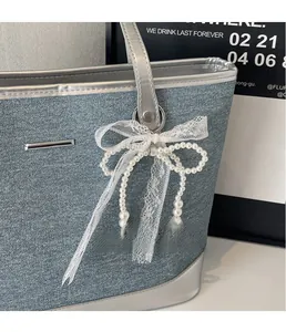 Détail du charm nœud en perles et ruban de dentelle blanche sur sac cabas en denim
