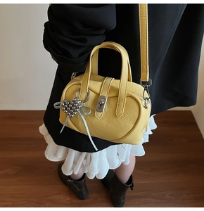 Detail of yellow pebbled leather crossbody bag with heart pendant and silk ribbon