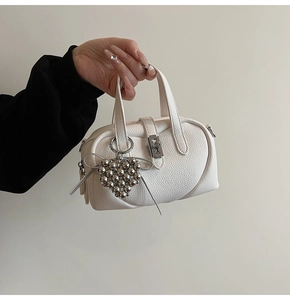 Detail of white lychee leather handbag with silver heart charm and bow accent