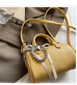 Détail du sac oreiller en cuir jaune avec nœud en ruban et breloque cœur argenté