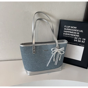 Détail du sac cabas en denim bleu avec anses argentées et pendentif en dentelle perlée