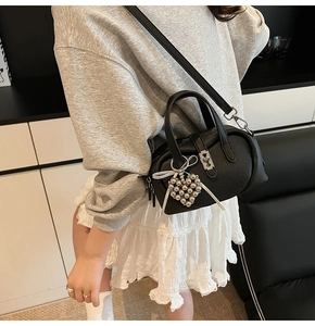 Detail of black lychee grain leather handbag with silver heart pendant and white silk bow