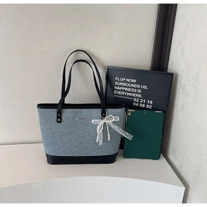 Détail du cabas contrasté en tissu gris, cuir noir et breloque noeud en perles