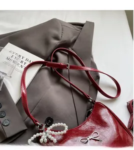 Close-up of red oil wax leather handbag with silver bow and pearl charm on gray suit