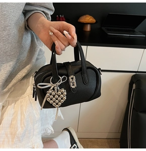 Close-up of black lychee grain leather mini bag with silver heart charm and white ribbon