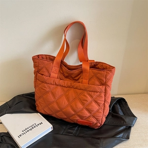 Vibrant orange quilted tote bag with wide strap on a stylish dark background