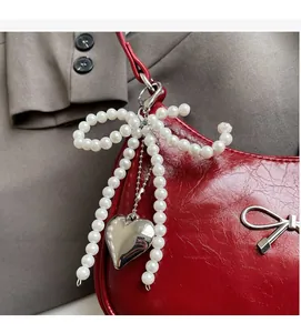 Detail of pearl bow charm and metal heart pendant on a red textured handbag strap