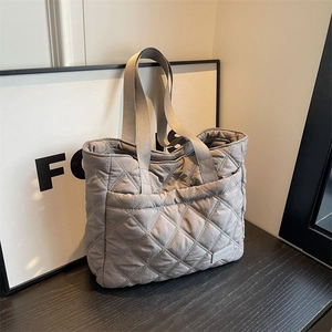 Grey quilted tote bag with diamond stitching and wide handles on dark wood surface
