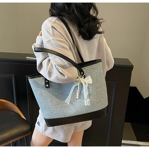 Détail du sac cabas bicolore avec un élégant nœud en dentelle et pendentif en perles