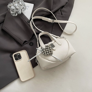 Detail of white litchi leather Boston bag with metallic heart charm and slim strap