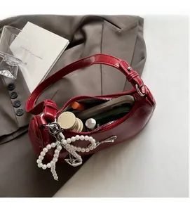 Detail of red patent leather handbag with silver bow and pearl charm showing interior capacity